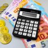Calculator with euro banknotes and cryptocurrency coins like Bitcoin on a table.
