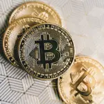 A close-up image of gold Bitcoin cryptocurrency coins on a geometric patterned surface.